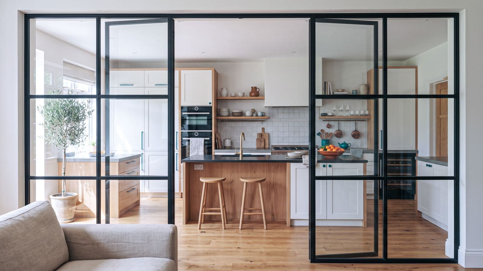 Cuisine semi-ouverte avec verrière d'atelier en bois clair séparant la pièce du salon