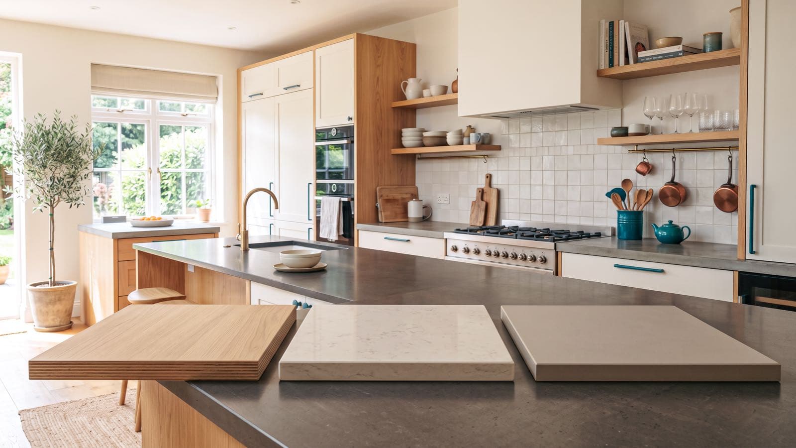 Trois échantillons de plan de travail, stratifié bois clair, quartz gris veiné et céramique blanche mate, posés côte à côte